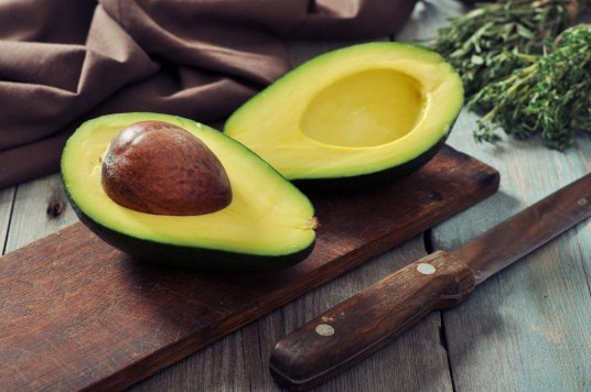 2 halves of avocados one with its seed and one without seed are layed beside each other with a knife 