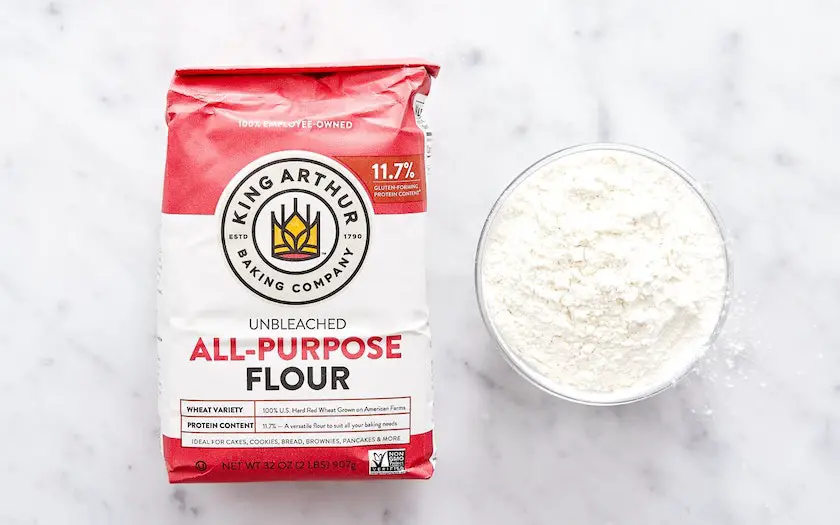 a bag of king arthur all purpose flour beside some flour in a small bowl