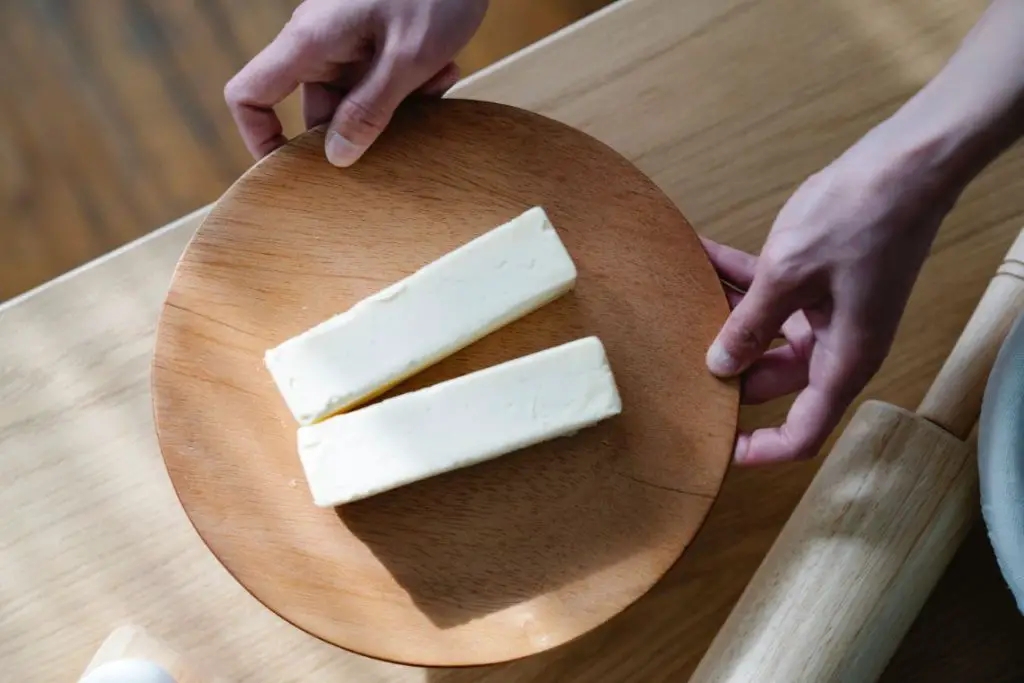a person holding a wooden plate with sliced zero-calorie butter on it