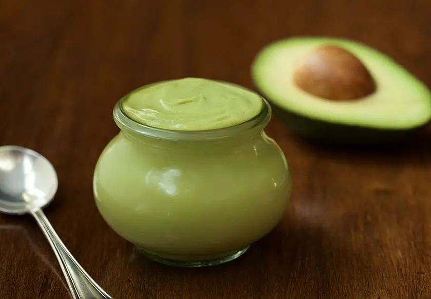 avocado mayonnaise in a mini glass jar along with a spoon and a half of avocado