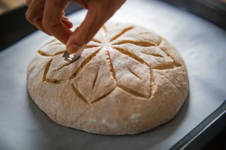 a woman scoring bread dough by using a blade 