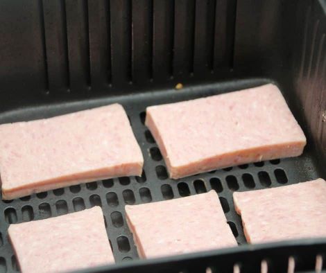 slices of uncooked spam on the air fryer basket -  air fryer spam