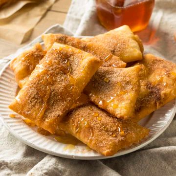 sopapillas drizzled with honey served on a white plate - Air Fryer Sopapillas 